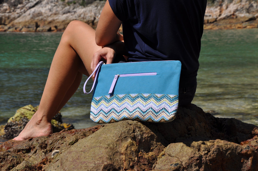 woman at the beach with her blue, teal and purple cosmetic travel bag