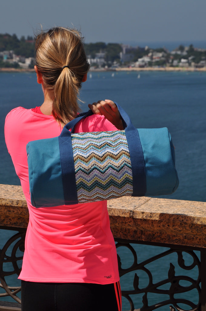 Girl watching the sea and carrying a blue canvas and nylon gym bag